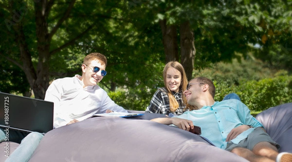 Fototapeta Three happy smiling young friends laying on a cushion outdoors and looking at each other.