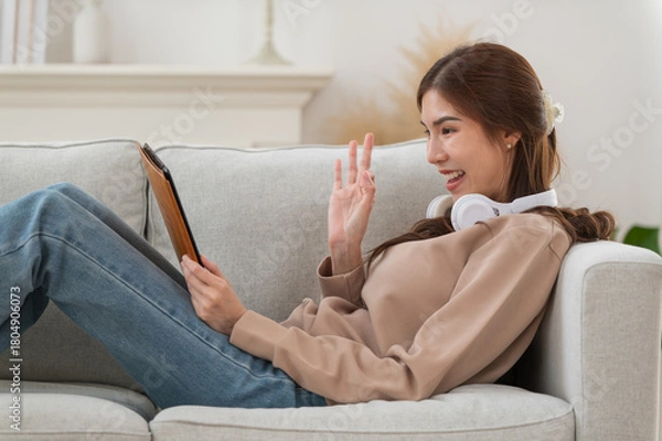 Fototapeta Young Asian woman enjoy listening to music with headphones while using digital tablet in the modern living room at home