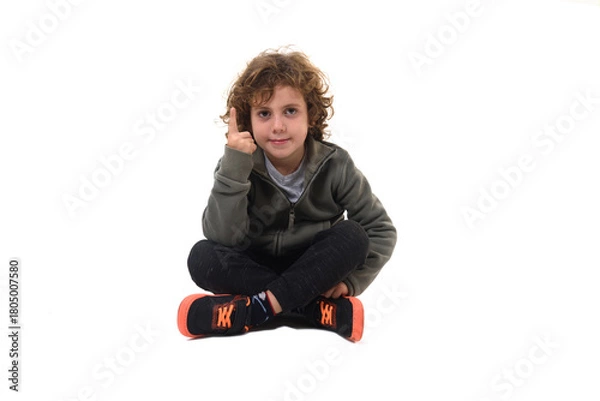 Obraz front view of  boy dressed in sportswear sitting on the floor looking at camera pointing up on  white background