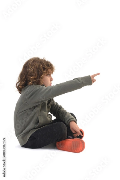 Fototapeta side view of  boy dressed in sportswear sitting on the floor pointing on white background