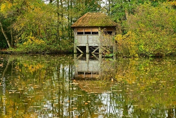 Fototapeta Thatched Hut on Stilts Reflected in Autumn Forest Lake