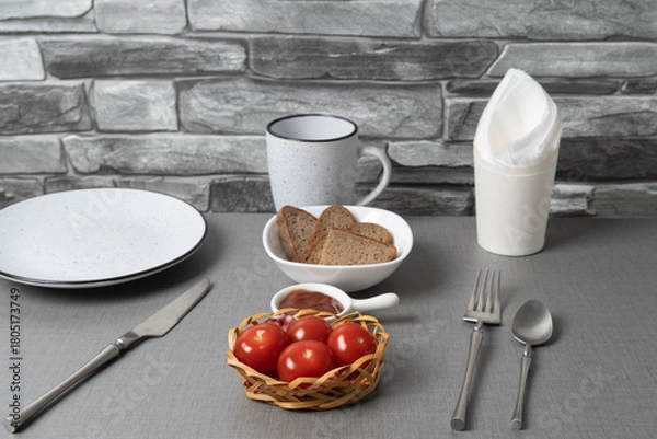 Fototapeta Fresh red tomatoes in a woven basket with snacks and drinks on a gray table in a cozy kitchen setting
