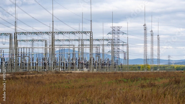Fototapeta Electrical power substation and high-voltage transmission towers in a rural field, symbolizing energy distribution, infrastructure, and technology.