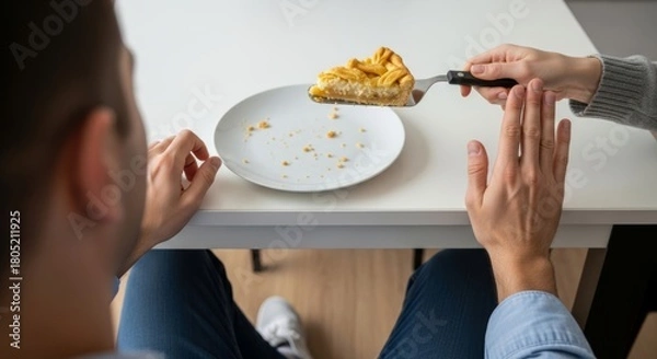 Fototapeta A man makes a stop gesture with his hand to refuse a slice of pie being offered by a woman. An over-the-shoulder view shows his empty plate with crumbs.