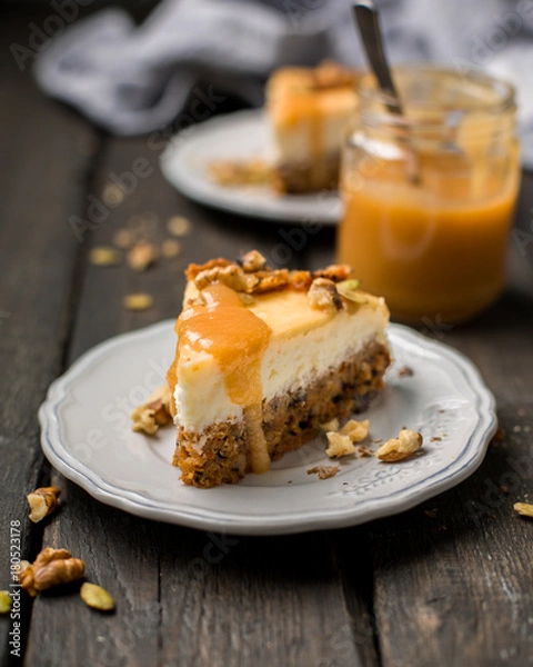 Obraz Carrot nut vanilla cheesecake with salty homemade caramel on a white plate on a dark wooden vintage background. Two pieces of homemade cheesecake. Caramel sauce in a jar.