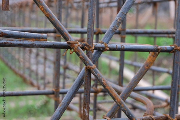 Fototapeta A close-up view of a rust-textured steel rebar frame used for house foundation construction, tightly tied with wire to form a strong structural grid.