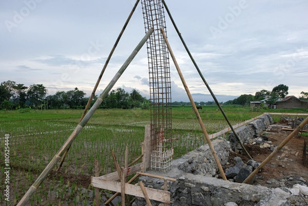Fototapeta A close-up view of a reinforced steel column frame partially covered in fresh concrete at a house construction site, showing the early stage of foundation and structural work.