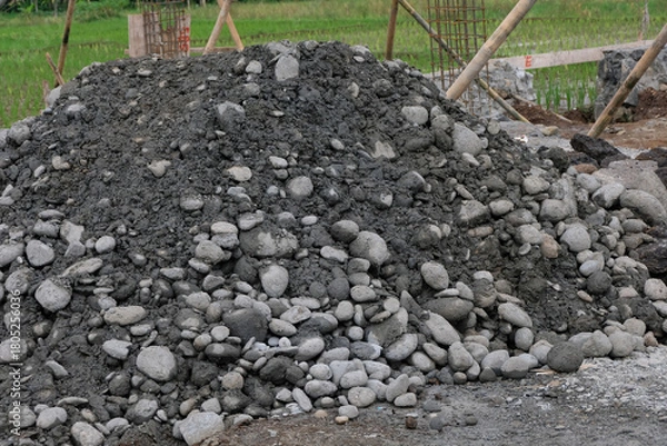 Fototapeta A pile of construction materials, including gravel and soil, at a house-building site with reinforced steel columns and wooden supports visible in the background.
