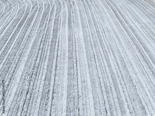 Fototapeta Aerial drone view of a plowed agricultural field covered in fresh white snow featuring rhythmic linear patterns and winter texture.