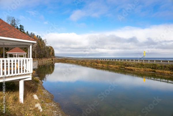 Fototapeta A serene rest stop in Quebec showcasing tranquil reflections, lush foliage, and an inviting gazebo under a vast sky.