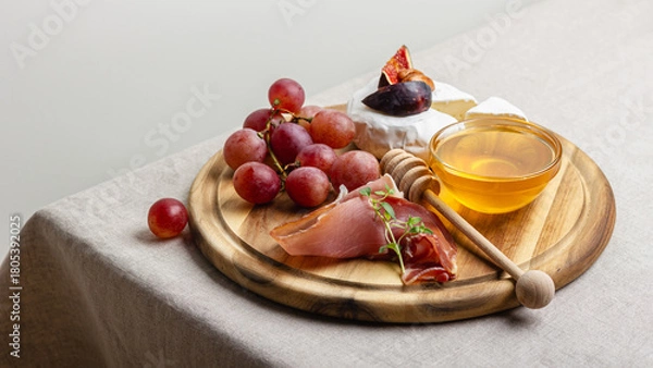 Obraz Appetizer board with meat, cheese, grapes, nuts, honey and fresh figs.