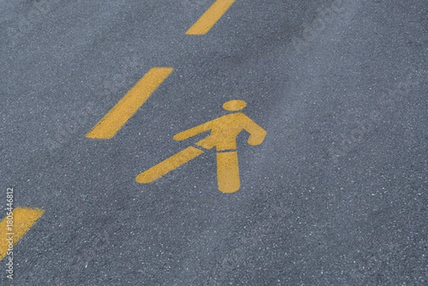 Fototapeta yellow pedestrian symbol is painted onto the dark gray asphalt surface. road pavement also features two parallel, dashed yellow lines, indicating a designated walking lane or crossing zone.