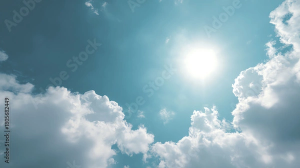 Fototapeta Bright sun shining through fluffy clouds in a clear blue sky, creating a serene and uplifting atmosphere.