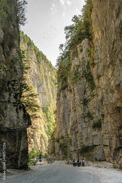 Fototapeta Bicyclists on asphalt road through gorge along Bzyb river near Ritsa lake in Abkhazia