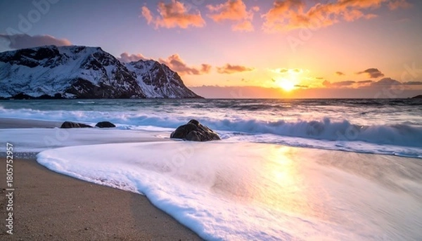 Fototapeta A sunset view of waves washing onto a sandy beach with snow-covered mountains in the background