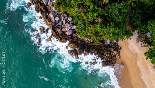 Fototapeta Aerial shot of turquoise waves crashing on a sandy shore next to rocky cliffs covered in lush green trees