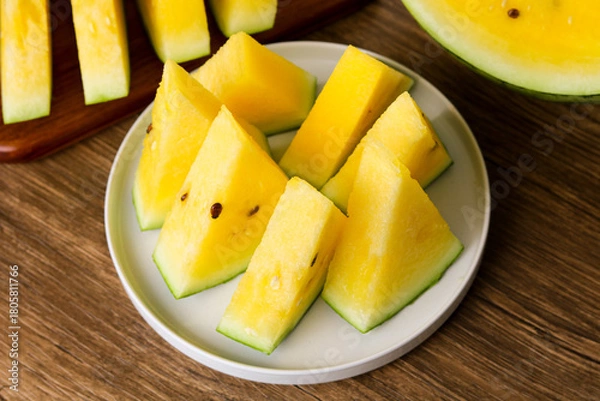 Fototapeta Closeup of freshly sliced yellow watermelon wedges arranged on a plate, showcasing their vibrant golden flesh and crisp green rind.