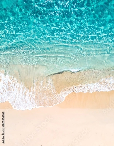 Fototapeta Aerial view of crystal clear turquoise ocean waves lapping onto a light beige sandy beach shoreline