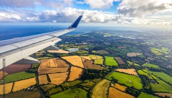 Obraz Aerial view of patchwork fields and coastline seen from plane window under sunny, partly cloudy sky