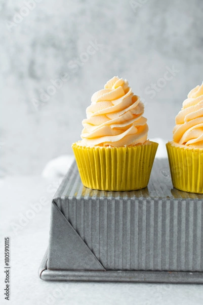 Obraz yellow cupcake with orange buttercream frosting on white background, tall buttercream frosting on yellow cupcakes