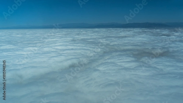 Fototapeta The solid surface of the clouds is visible from the airplane window. Mountains on the horizon. The blue sky. Peru