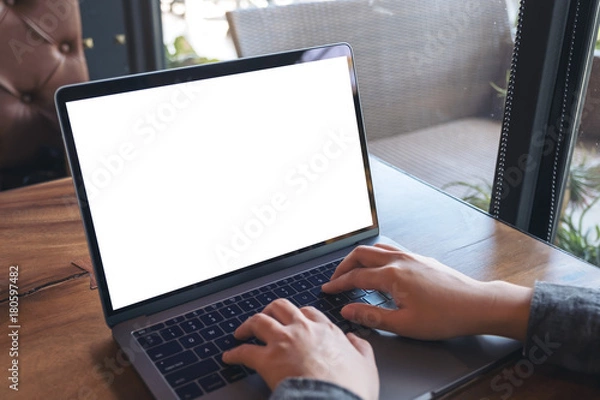 Fototapeta Mockup image of business woman using and typing on laptop with blank white screen on wooden table in cafe