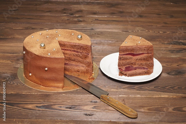 Obraz A confectionery product. A chocolate cake with a cut-out slice on a golden base, on a wooden table.