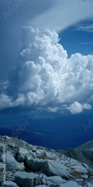 Fototapeta Majestic cumulonimbus clouds dominate a vast blue sky above a rugged rocky mountain summit overlooking a distant valley