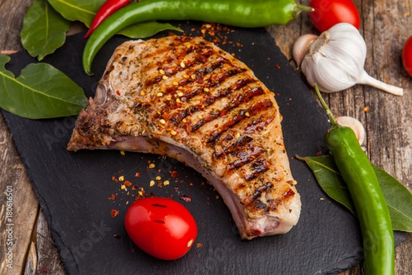Fototapeta Grilled pork steak on the bone with seasonings and grilled tomatoes on a black background. Top view
