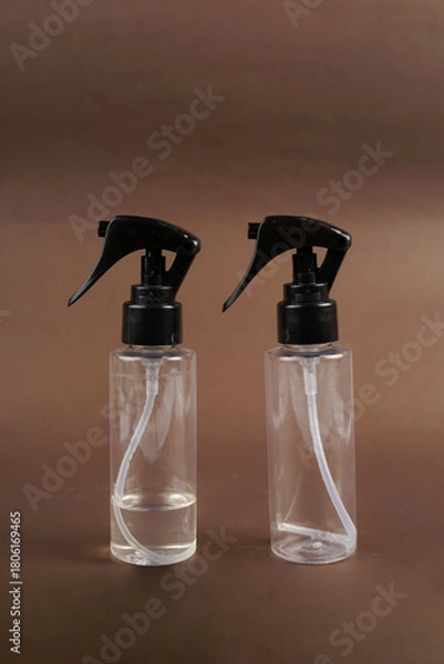 Fototapeta The rich brown backdrop enhances the sleek design of both spray bottles