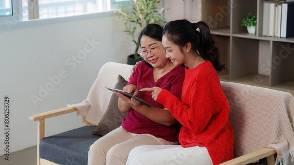 Obraz Shared joy. Mother and daughter exploring a tablet together in a cozy setting.