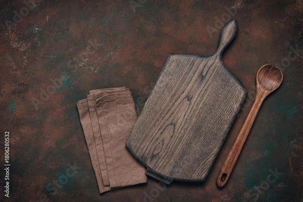 Fototapeta Culinary background with empty wooden cutting board, wooden spoon and linen napkin, dark brown grunge background, top view, flat lay, copy space