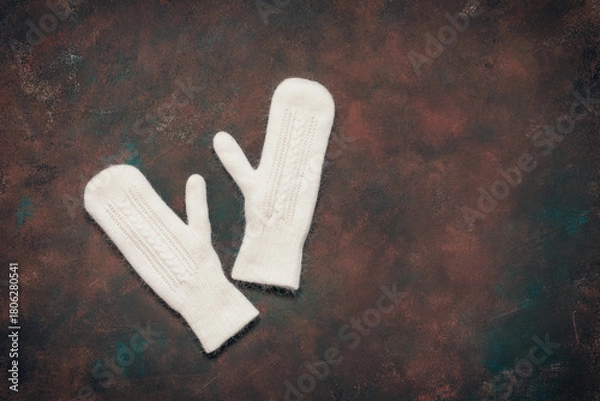 Fototapeta White fluffy knitted mittens on dark grunge background, top view, flat lay