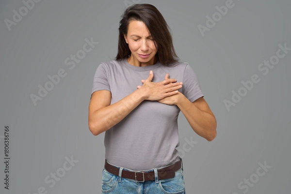 Obraz Woman holding chest with both hands and eyes closed in discomfort, studio shot