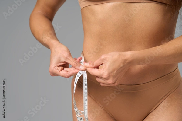 Fototapeta Close-up of woman measuring her waist with tape measure indoors