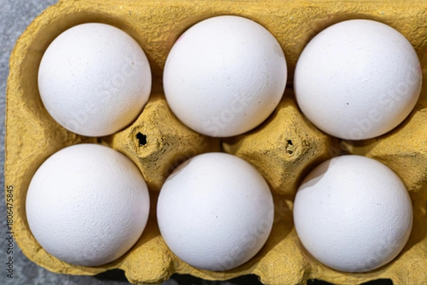 Obraz Fresh white eggs in a yellow carton ready for cooking or baking on a kitchen countertop