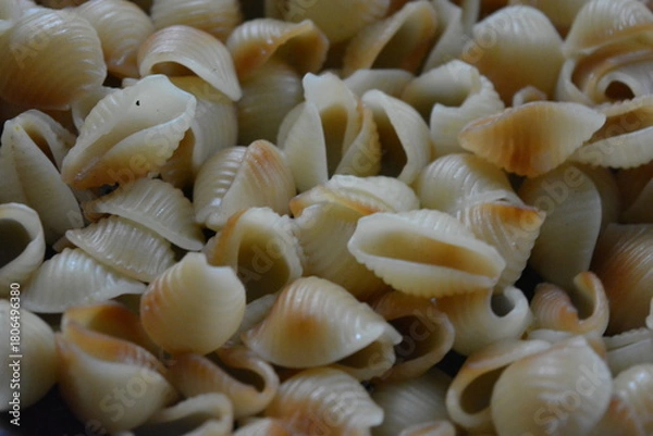 Fototapeta Food, cooking in a home kitchen. Boiled vermicelli, shaped like brown, black, yellow shells lies in an old, thick frying pan.