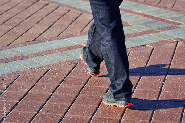 Fototapeta Feet in warm winter boots walking across paved sidewalk covered with scattered salt crystals on sunny cold day, safety treatment used to prevent slipping on icy urban surfaces in winter season