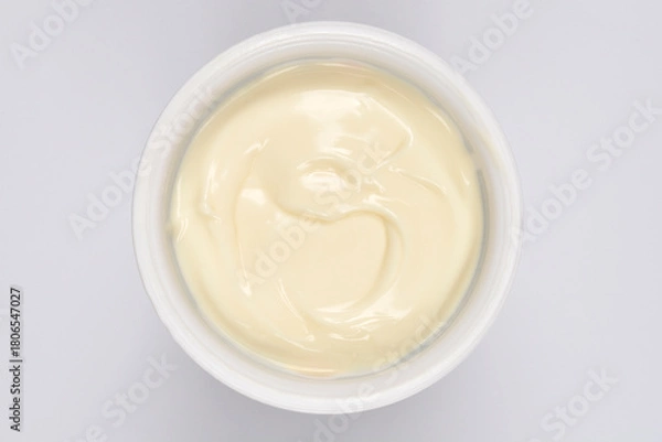 Fototapeta A creamy white chocolate pudding in a round plastic container is captured from a top-down view on a white background