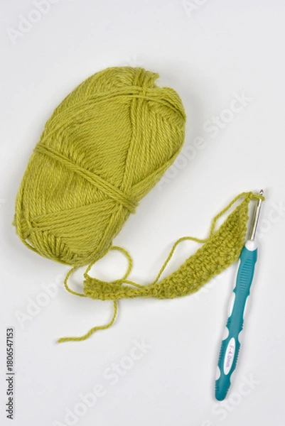 Fototapeta A ball of olive-green yarn, a crochet hook, and a small working swatch are displayed together on a white background