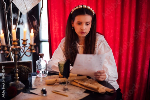 Obraz Young woman with long hair, wearing a white blouse, is reading a letter at a vintage table surrounded by candles and parchment, evoking a sense of nostalgia and mystery