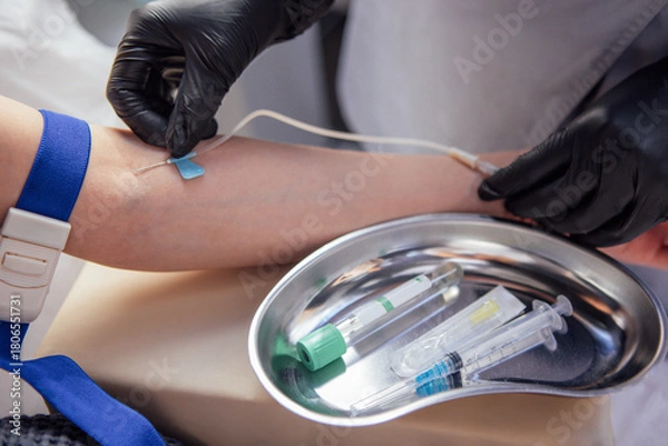 Fototapeta Medical professional in black gloves prepares to draw blood from a patients arm, showcasing medical tools and a sterile environment for healthcare procedures