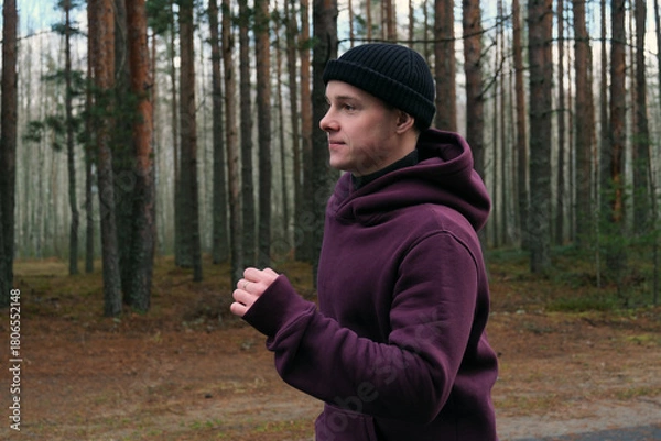 Obraz Man running in forest wearing hoodie and beanie