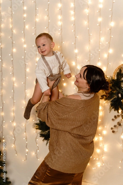Obraz Mother holding baby boy playing with him and tossing him around in New Year's room