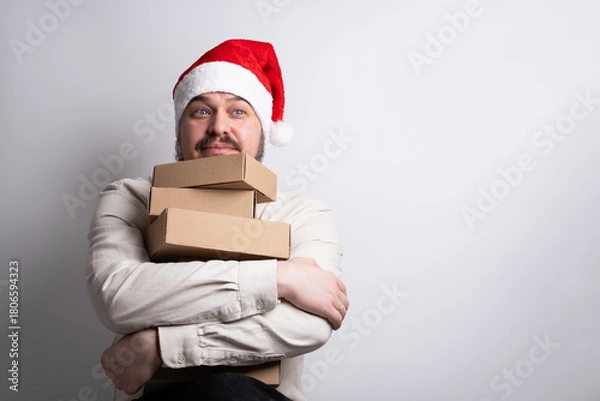 Obraz Happy man in santa hat holding stack of delivery boxes