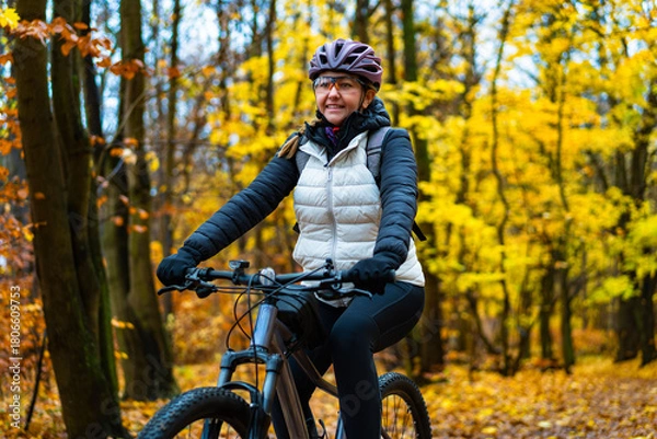 Fototapeta Beautiful middle-aged woman riding bicycle in forest in autumn. Front view	