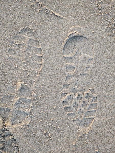 Fototapeta Footprints in soft sand along a beach at sunset reveal a journey by the shore