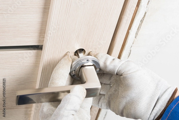 Fototapeta The master installs the door handle on the inner door to the house, close-up