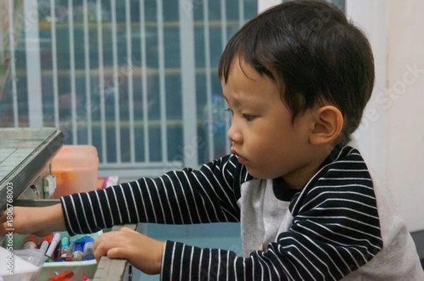 Obraz A young Asian child thoughtfully focused while holding objects