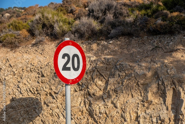 Obraz Speed limit sign near rocky hillside within bright sunlight, featuring dry shrubs above